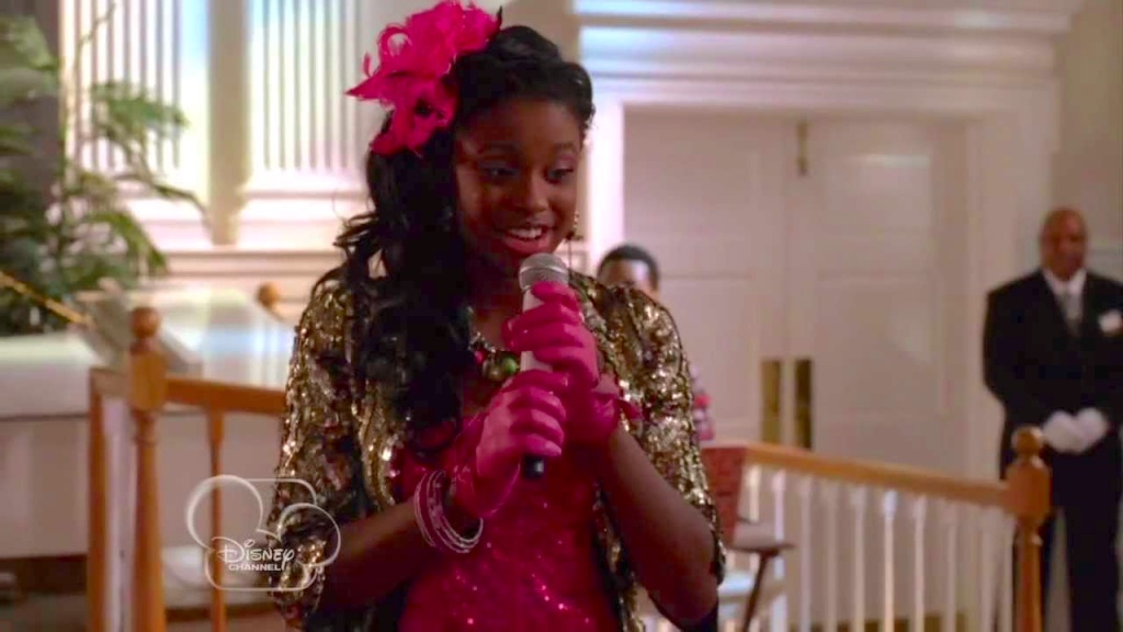 Roxie singing in Let It Shine. Pink dress, gold jacket, pink fascinator and gloves.